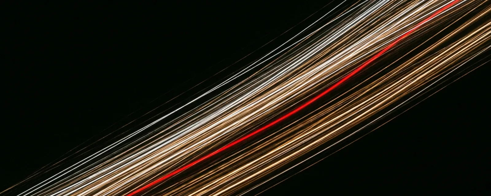 Rastros de luz em diagonal sobre fundo preto, com um único rastro vermelho entre os rastros claros